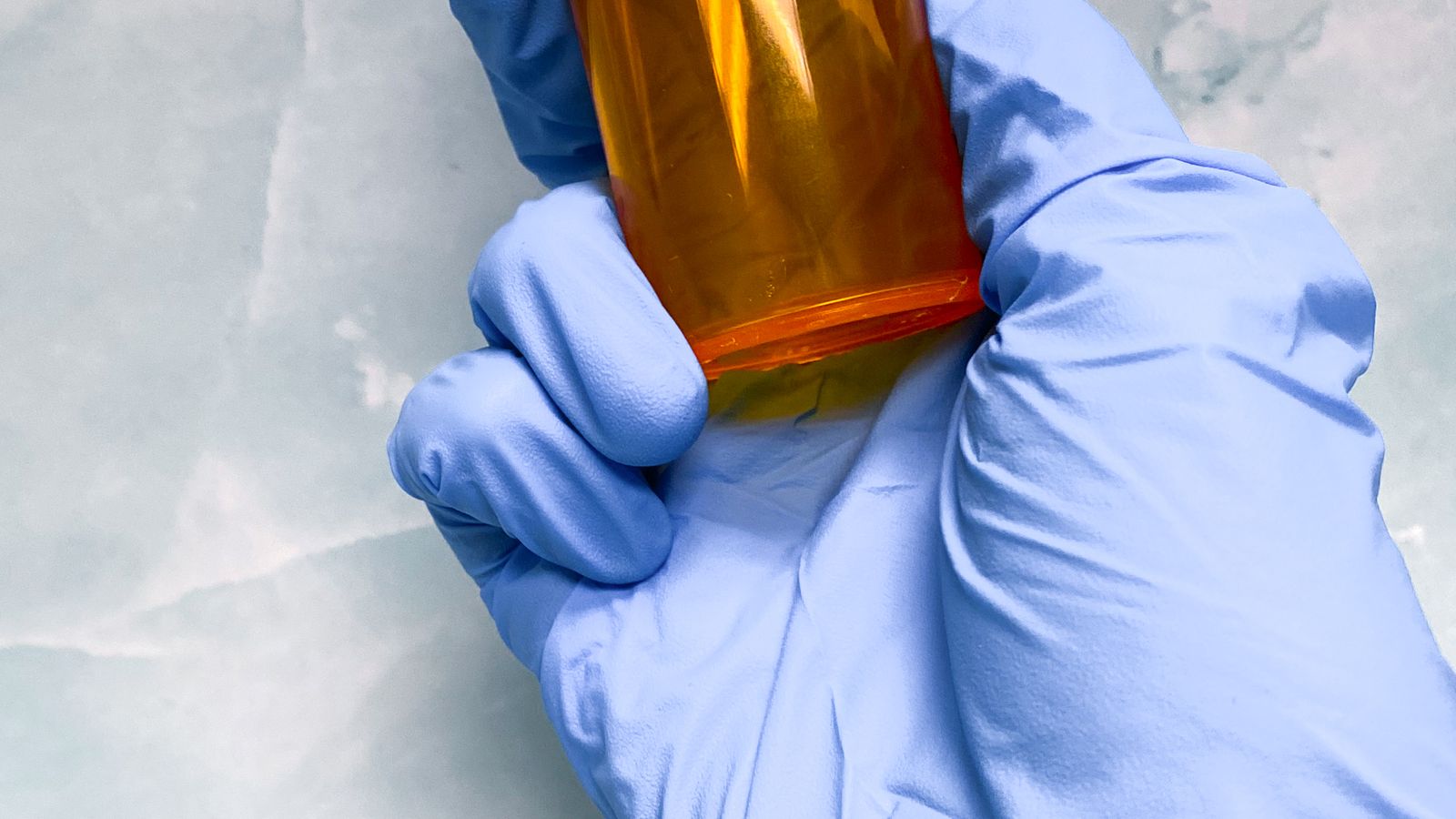 A gloved hand holds a small medication vial against a marble surface.